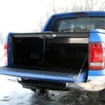 Blue truck with the tailgate down and a cover over the bed of the truck.